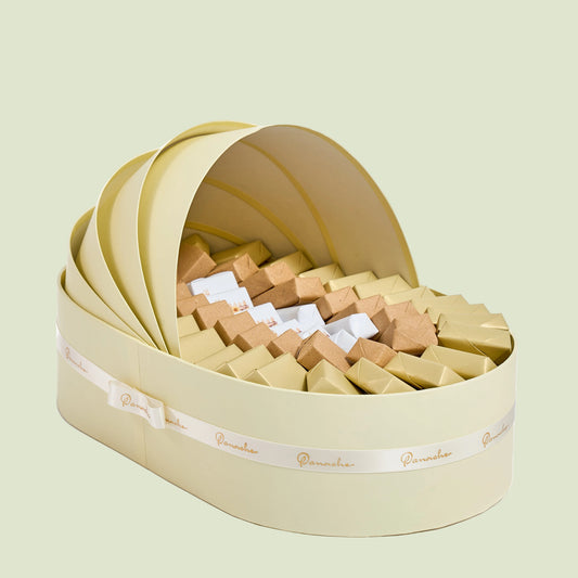 Ivory shell-shaped baby boy cradle gift box filled with assorted wrapped nougats side view"