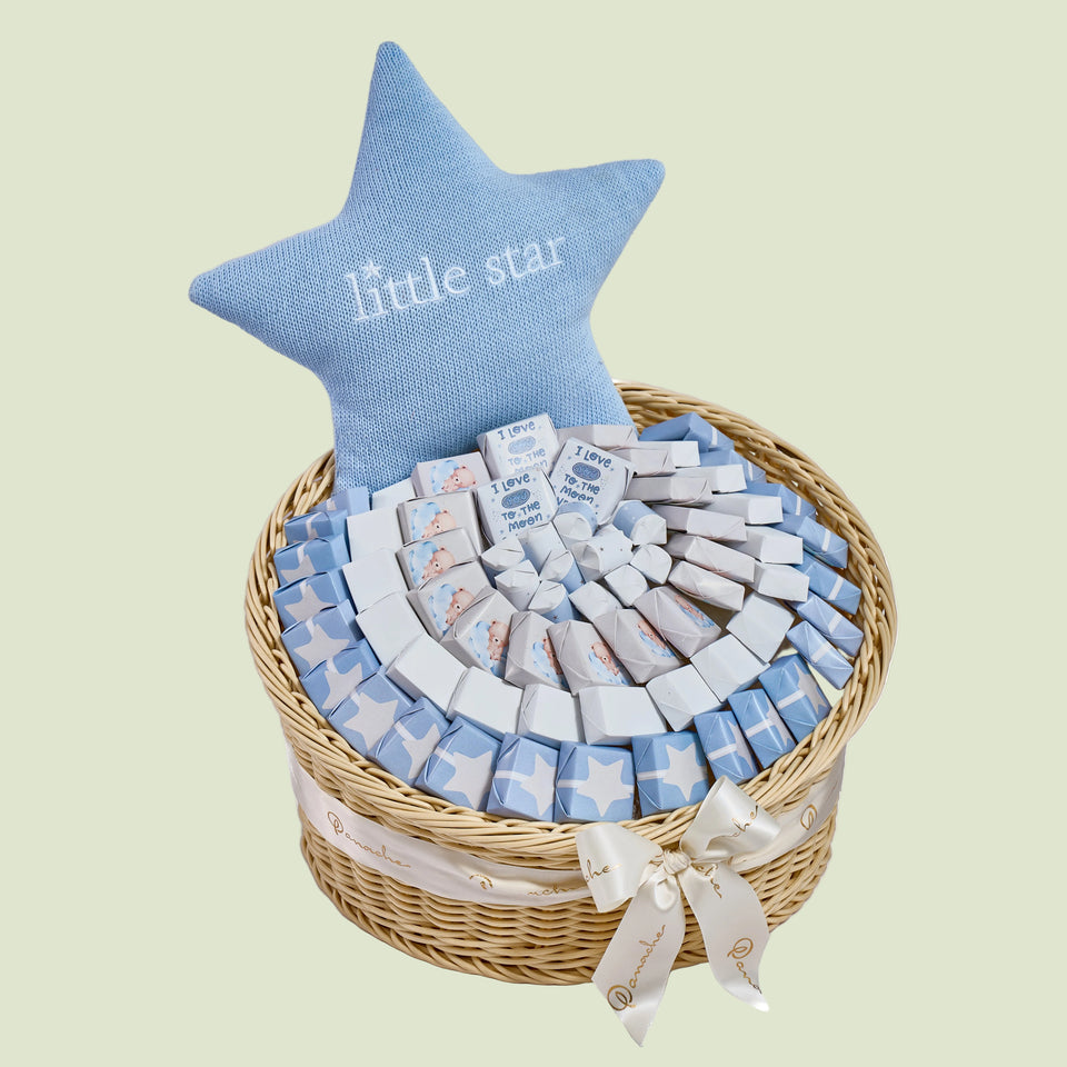 Baby boy star chocolate arrangement in wicker basket with blue star pillow and wrapped nougats